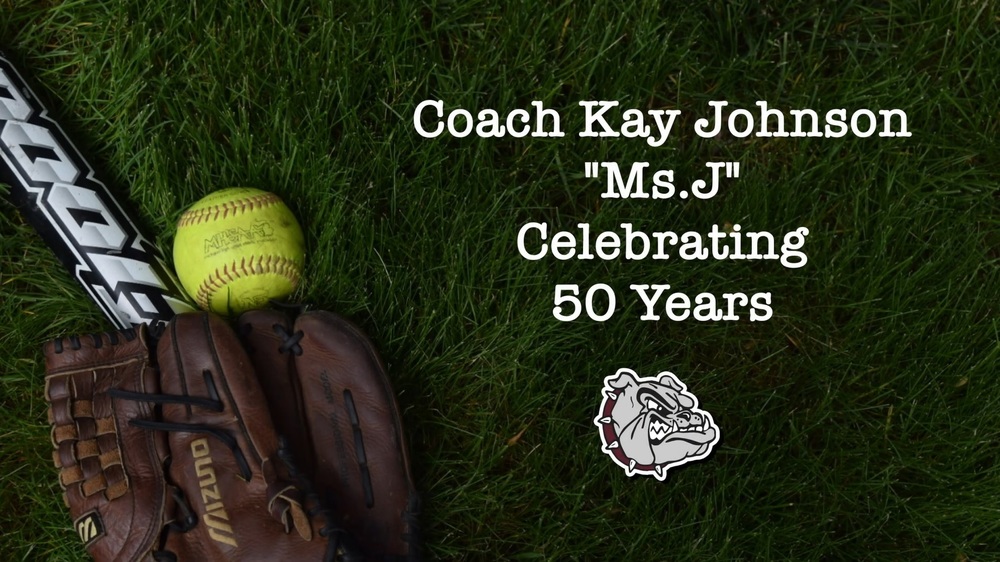 Grass background with a yellow softball, black and white softball bat and brown glove.  Coach Kay Johnson "Ms. J" Celebrating 50 Years.  The Morenci Bulldogs Logo is underneath.